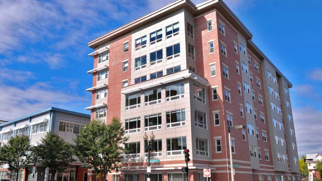 Modern 7 story brick building on a corner lot, beautiful trees.