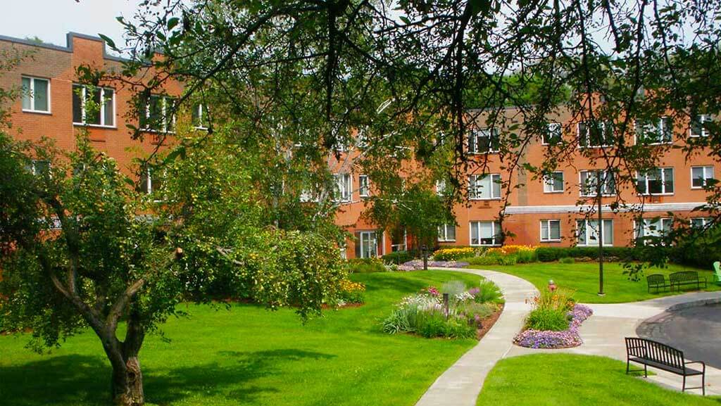 Brick apartment building in a beautiful landscaped setting, lots of green space.